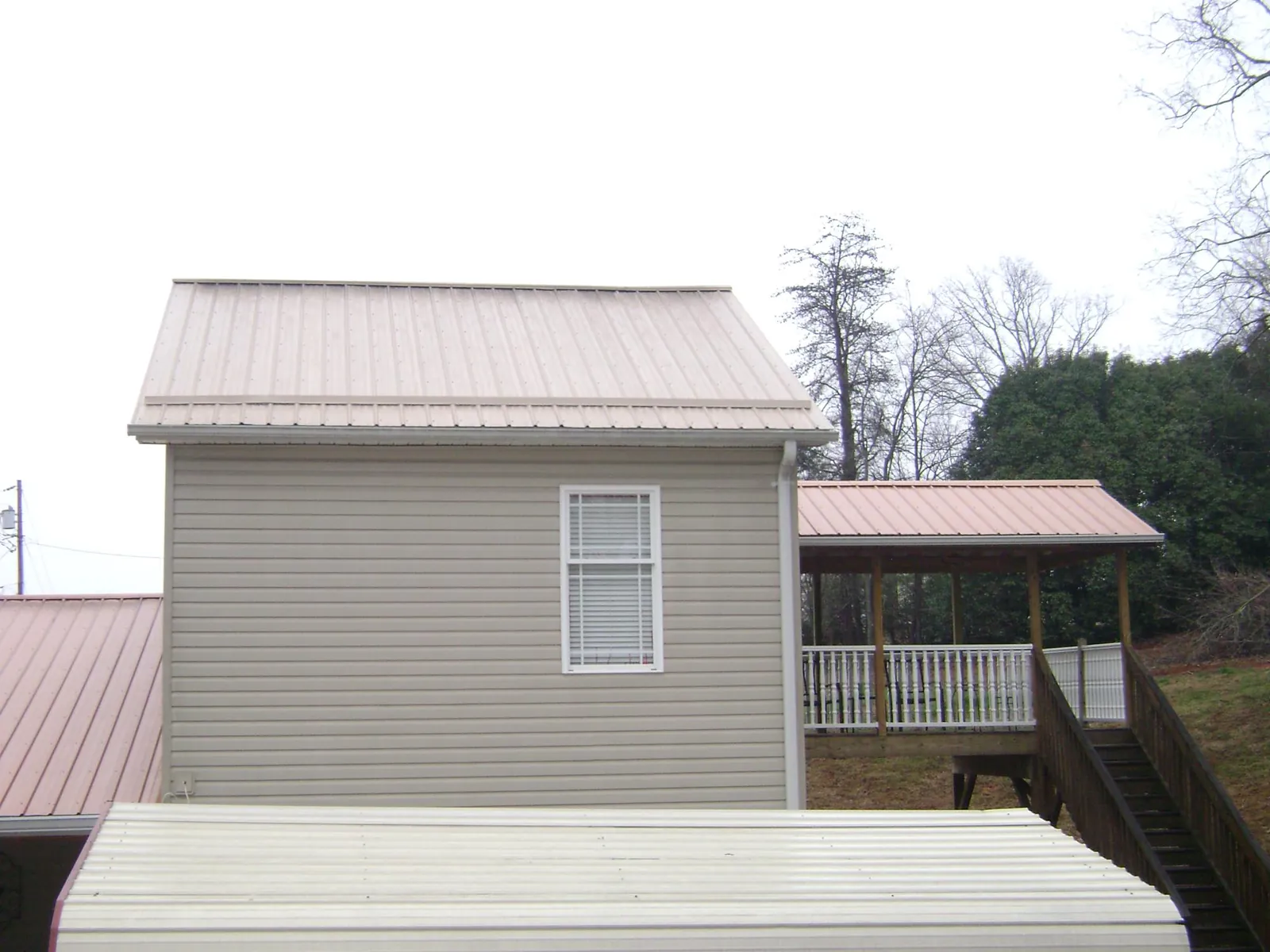 Tan metal roofs on a two story addition and attached porch, from a Roof Replacement job in Ivanhoe